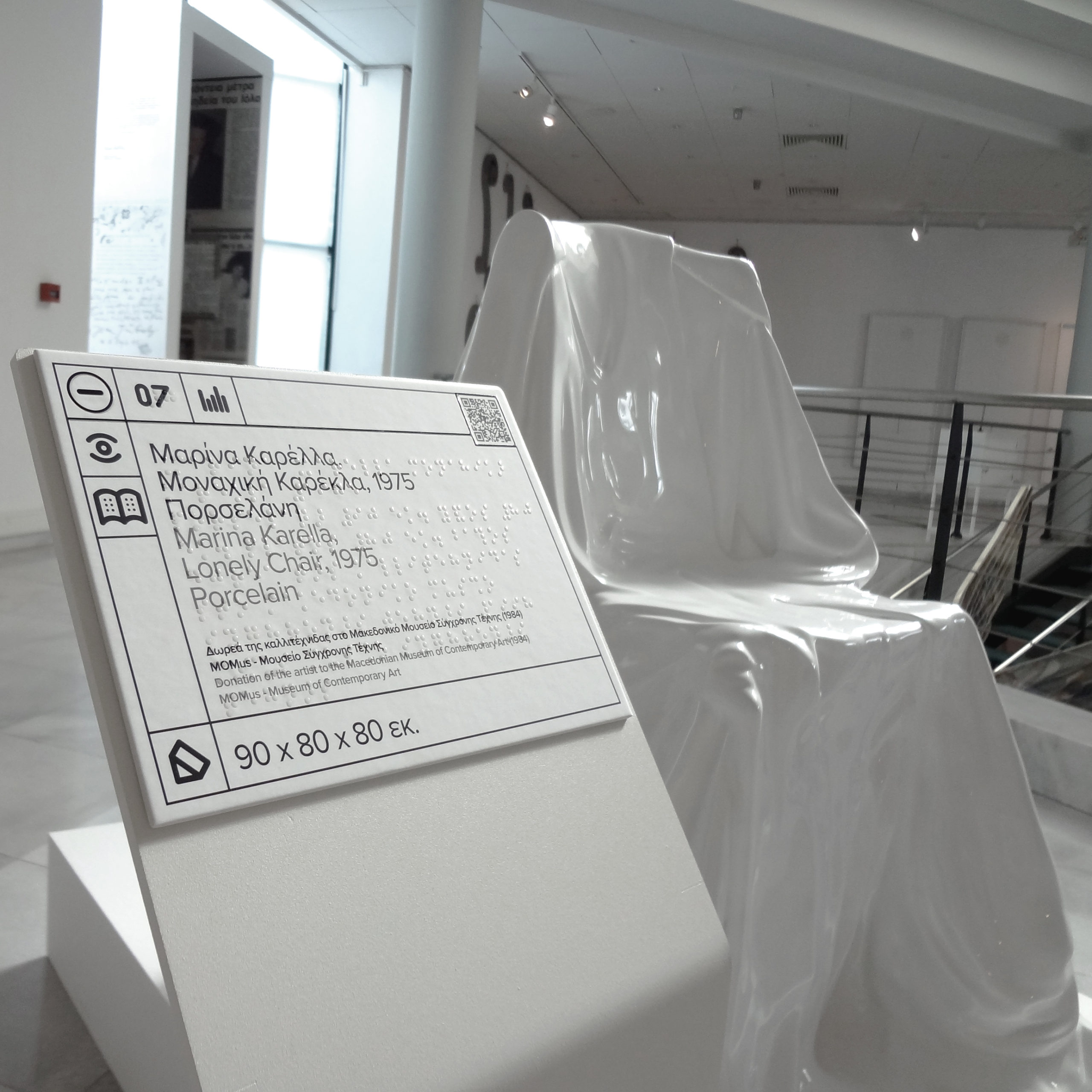 Στο πρώτο πλάνο της εικόνας φαίνονται λεπτομέρειες από τη λεζάντα του έργου και στο βάθος διακρίνεται το έργο τέχνης.